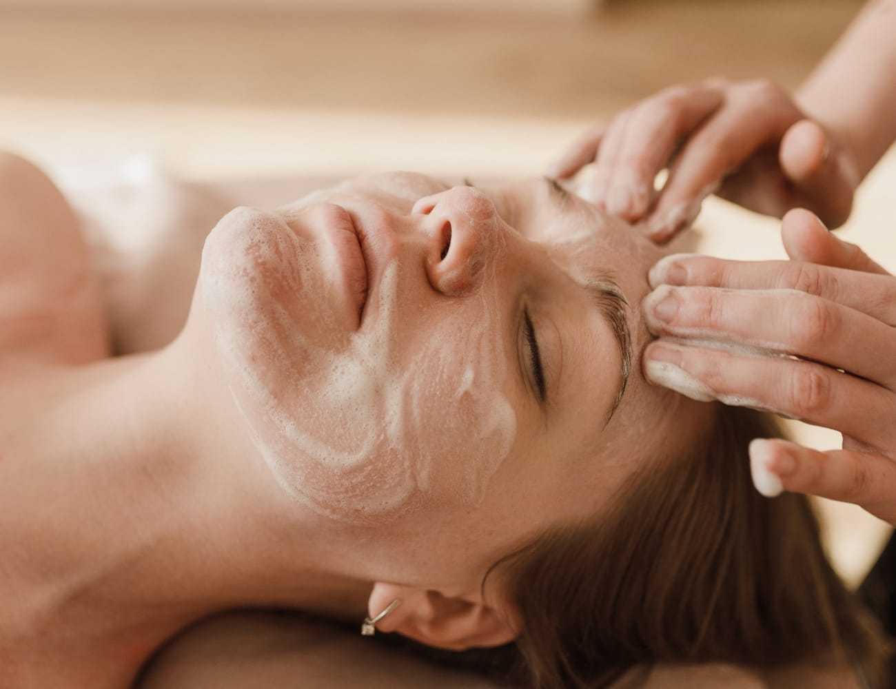 A person receives a relaxing facial massage with a foamy cleanser applied.