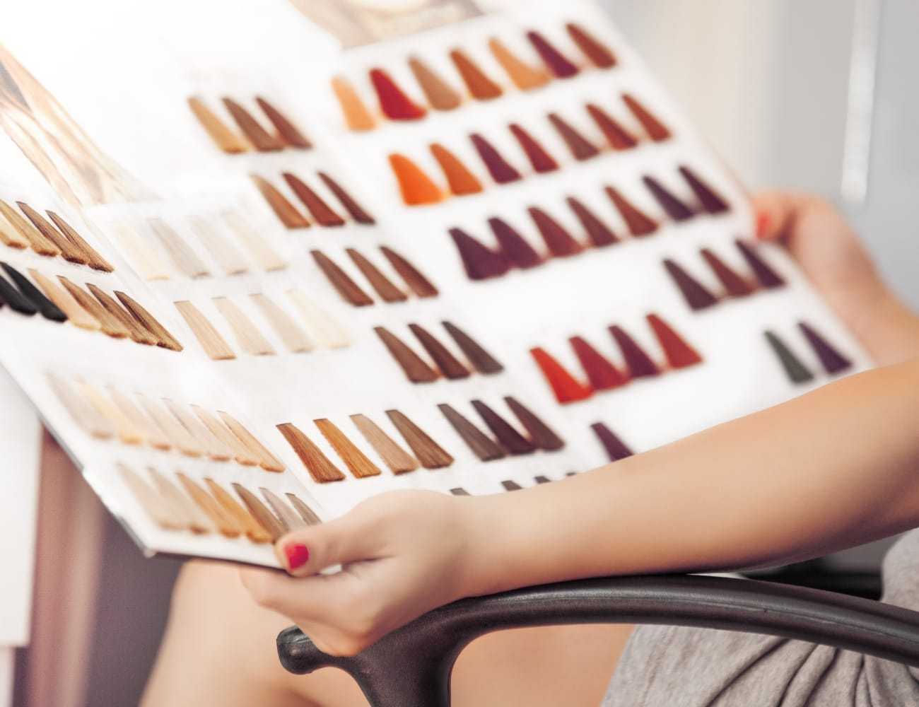 Person holding a book of hair color samples, showcasing various shades in a salon setting.